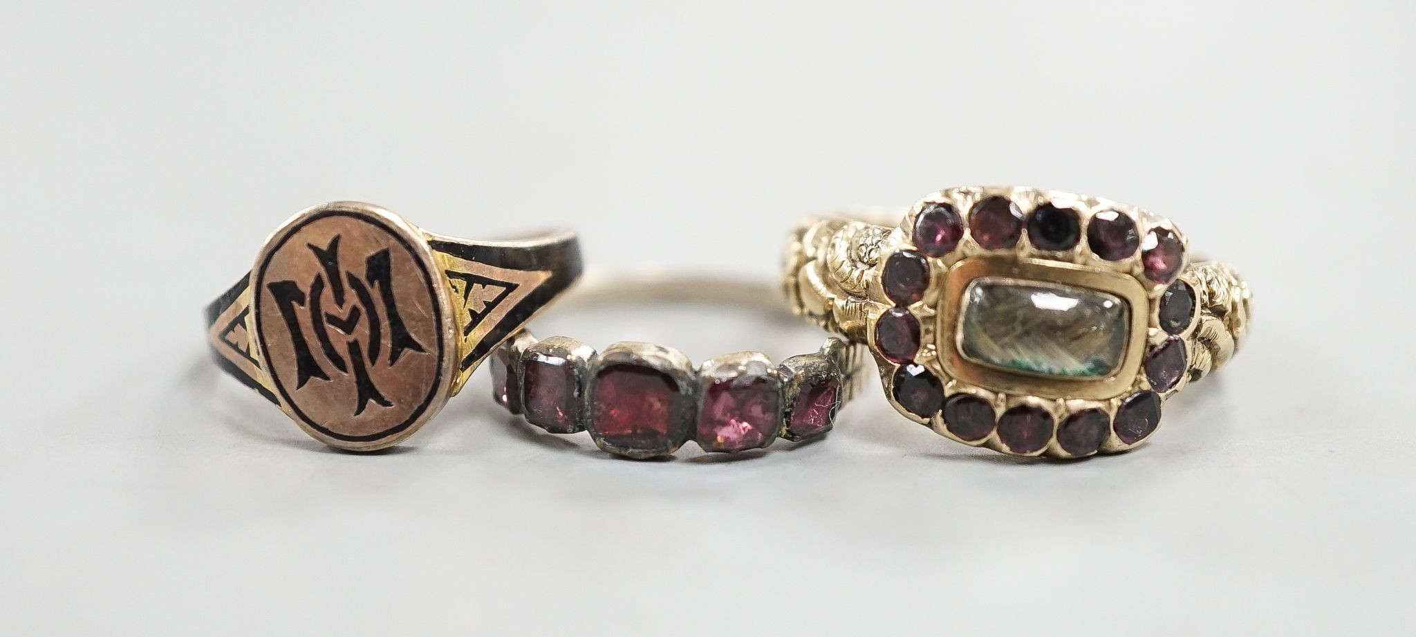 A late George III yellow metal, garnet and plaited hair mounted mourning ring, inscribed 'Ann Haycock Obt. 1 Mar. 1817 at 25, Mary Haycock ob, 26 Mar, 1817 at 15' size N/O, gross 4.6 grams and two other antique rings.